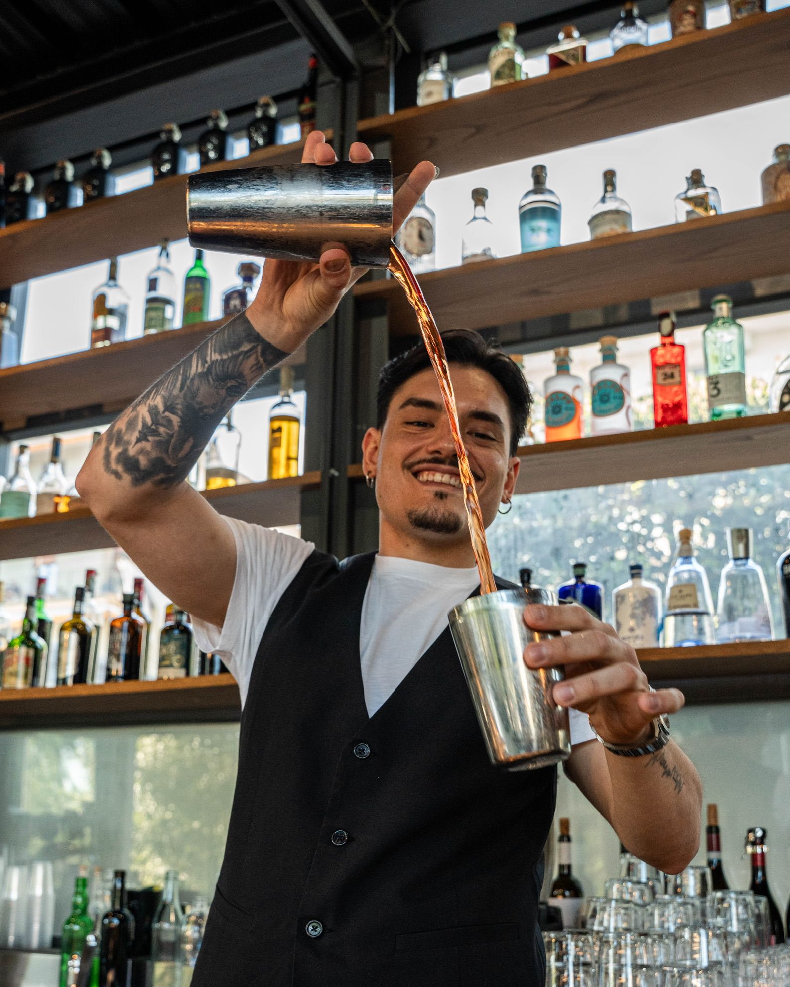 Cris Sola versa un cocktail dallo shaker dietro il bancone